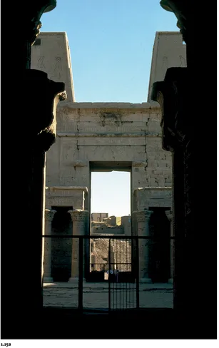 ›1.15 EDFU, TEMPLE OF HORUS, c. 250–116: (a) view along the main axis from the hypostyle hall, through the forecourt to the entrance between the twin pylons, (b) detail of columns and beams in the hypostyle hall at the head of the inner court. In this typical Ptolemaic Egyptian cult temple, the six columns of the hall façade, screened to half-height, and the twelve larger interior columns have a variety of capitals ranging from the traditional palm-frond bundle (background) to variations on the lotus theme (foreground).