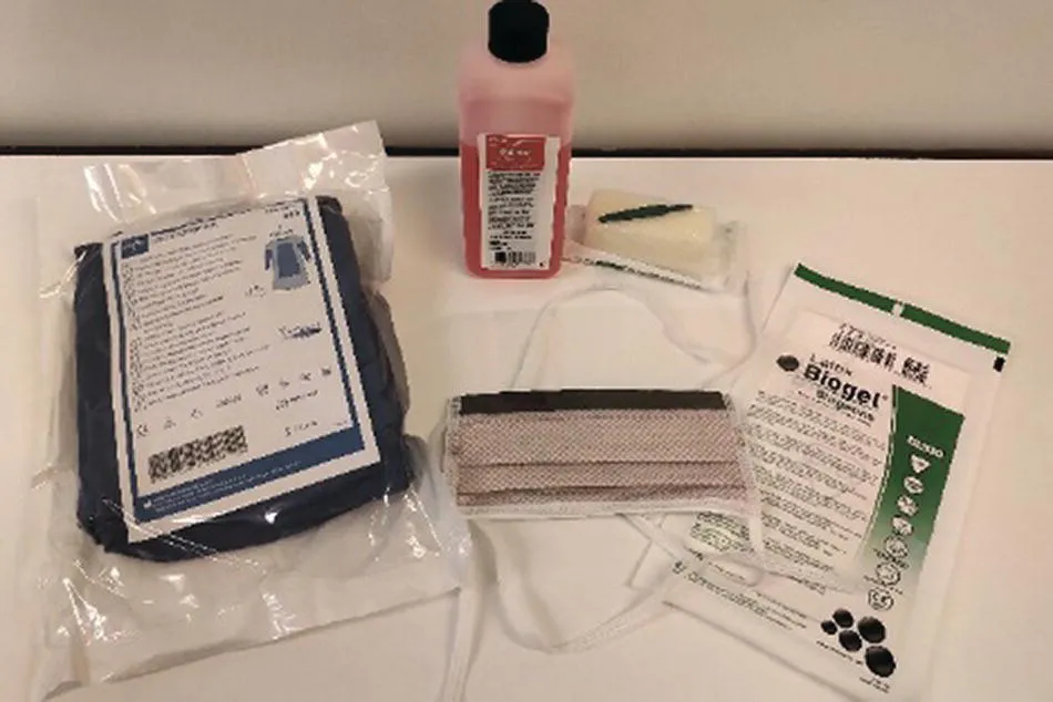 Photo displaying a bottle of antiseptic solution, a gown, gloves, a face mask, and a nail brush.
