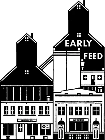 A grain elevator consisting of two buildings, the right one taller than the left. “Early Seed” is written on the right building and both buildings have signs saying “Early Seed and Feed” above the doors.