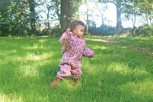  One toddler walking unsteadily through grass in a natural landscape.