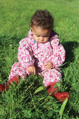  One toddler sitting in the grass, touching grass.