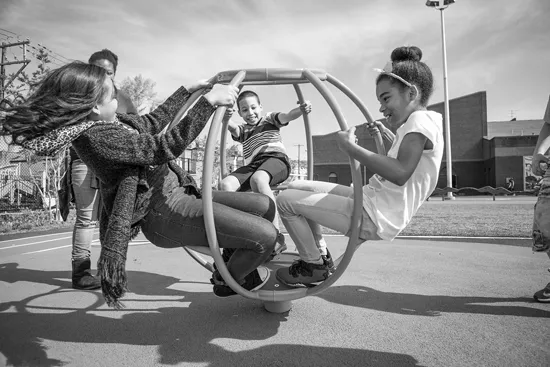 A small group of students play on an outdoor playground structure on a sunny day.