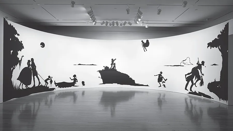 Silhouettes of women, men, children, and landscape elements cut out of black paper on curved wall as part of museum installation.