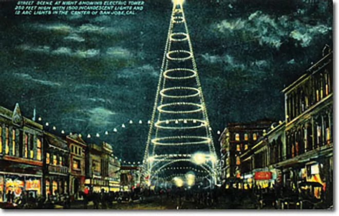 The postcard shows a light tower taller than adjacent downtown buildings with light bulbs on horizontal loops and on all vertical poles.