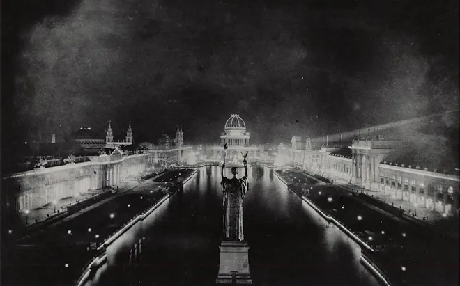 The historic postcard shows a statue in the foreground, a long reflecting pool surrounded by brightly lit long buildings, with domed buildings in the background.