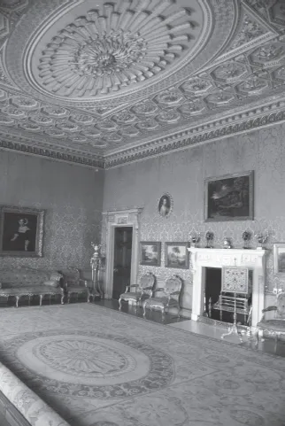 Formal parlor of 1770s English mansion with ornate ceiling medallion, rug, fireplace, silk wallcloth, and gold painted chairs