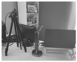 At home interactive virutal learning set up consisiting of a desk with display screen and laptop on it, tall greenscreen is behind the seat for the museum educator and a tripod holder for a camera is in front of the desk for museum educator to look into.