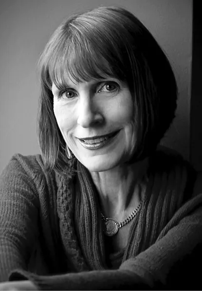 A woman with chin-length, brown hair smiles into the camera wearing a blue knit sweater.