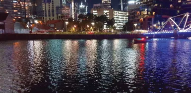 A photo shows the buildings, a bridge, and the street illuminated with bright lights, and the river flowing along the street reflects the different shades of lights.