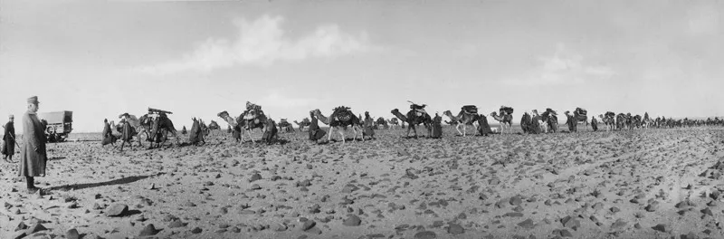 Deserto di Ben Afien, 7 dicembre 1913. Miani, con pastrano, osserva il passaggio della batteria di cannoni cammellata. (CMPA, s.f., foto n. 78)