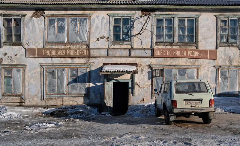Una casa fatiscente a Maldjak con i resti di uno slogan sovietico: LAVORATORI, QUI SI PRODUCE IL POTERE DELLA NOSTRA PATRIA!