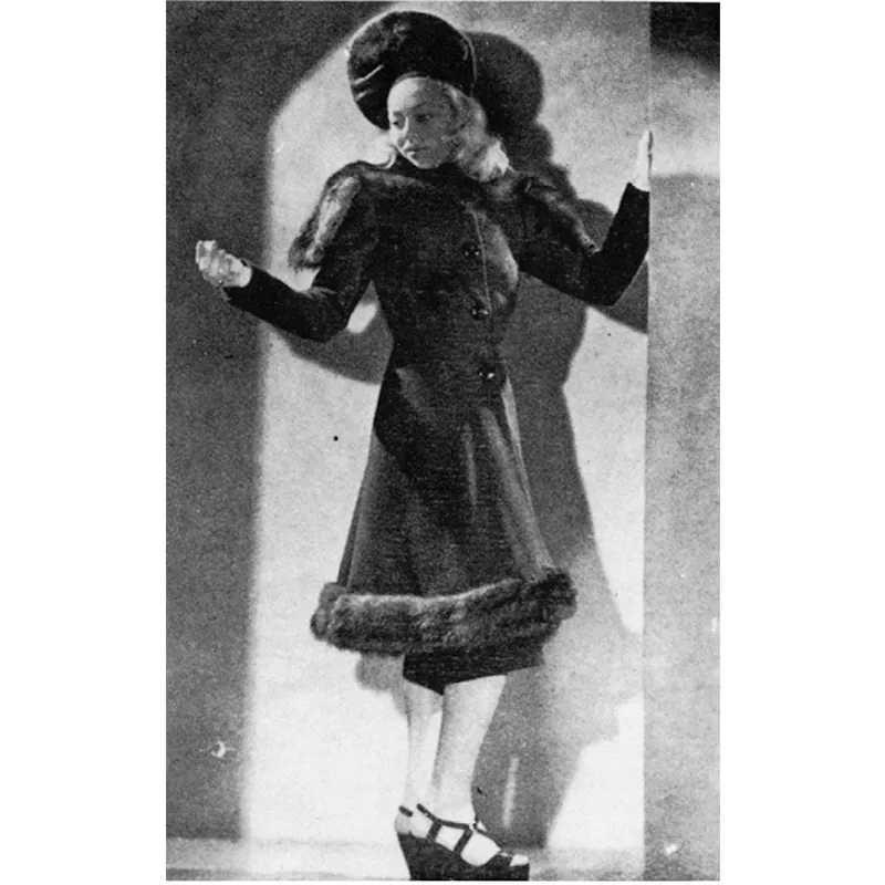 Di gusto vagamente militare la redingote avvitata, con decorazioni di pelliccia sulle spalle e all’orlo