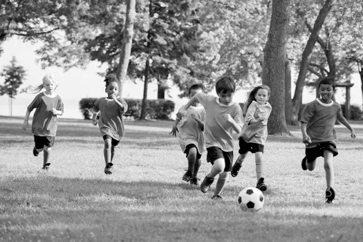 Multi-ethnic group of kids playing soccer together at the park.