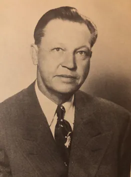 A headshot of Myford Irvine wearing a dark suit, white shirt and dark tie taken in the early 1940s