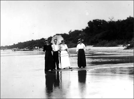 A black and white photograph showing one man and three women standing on a beach.