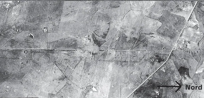 Fig. 2 - La Via Cassia nella pianura di Viterbo. Foto aerea della Royal Air Force che fotografò la superficie dell’Italia centrale nel febbraio del 1944, dopo lo sbarco degli Alleati ad Anzio e Nettuno. In orizzontale l’antico tracciato (che qui corre esattamente da nord a sud) interrotto al centro dell’immagine da fonti calde. Se in precedenza si è esplorato il terreno, gli edifici romani lungo la strada si riconoscono dalla loro ombra anche da 21.000 piedi d’altezza: monumenti funebri (tra i quali una tomba circolare chiamata Ruzzola d’Orlando), un tempio funerario e l’edificio a cupola di un grande impianto termale (sul margine a destra). In alto la strada per Marta.