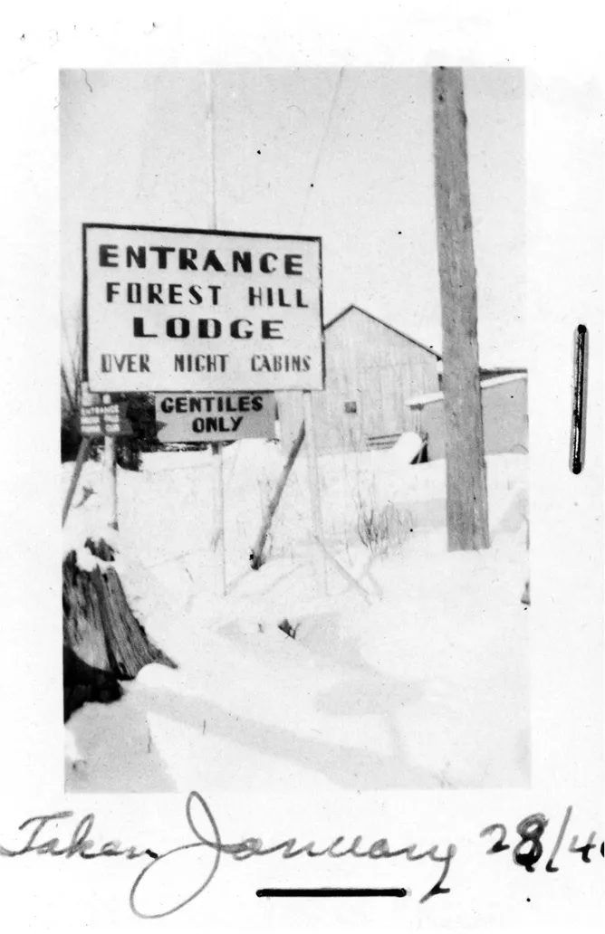 Large sign on fence outdoors reads Entrance forest hill lodge, over night cabins. Below a smaller sign reads Gentiles only.