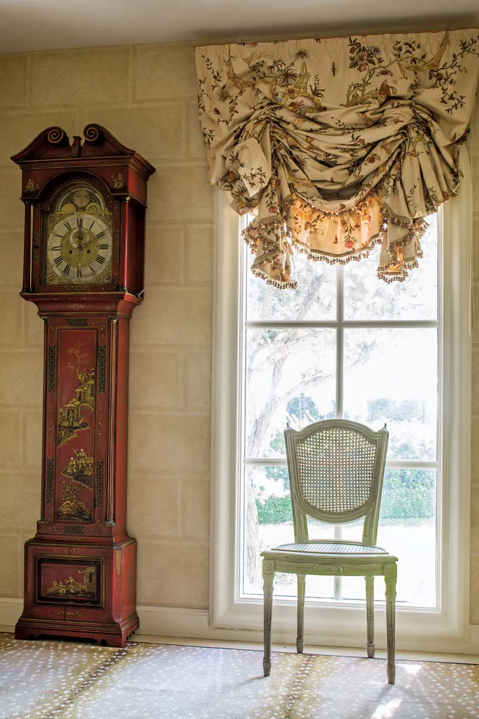A creamy chinoiserie from Clarence House complements the hand-stenciled ashlar block walls, a dash of red referencing the red-lacquered grandfather clock. The blind was softened with a self ruffle trim and delicate beading, which becomes lusher and fuller as it is raised.