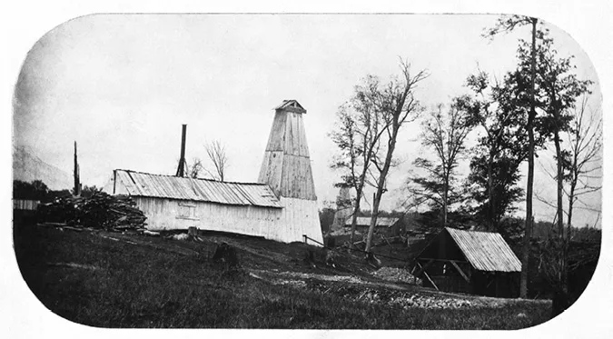 Photo shows tripods holding drilling rigs located behind a large shed.