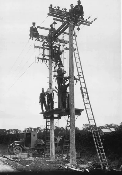 Picture taken sometime back in the year 1925 in New Zealand. Nine persons standing at different levels of a pole-mounted transformer substation construction site.