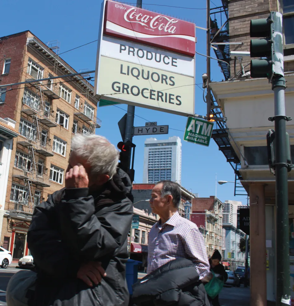 Photo of 2 men walking under a Coca-Cola advertising board under which are texts PRODUCE, LIQUORS, and GROCERIES.