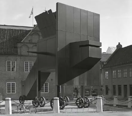 Photograph shows front view of a building with a flag placed on the roof.